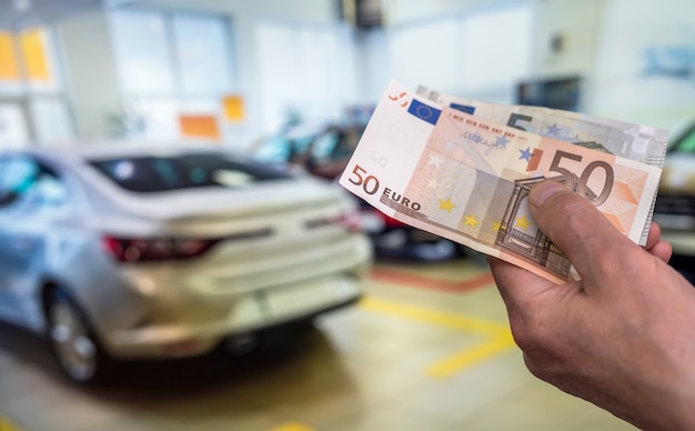 Mano sujetando los billetes en euros en la parte delantera del coche