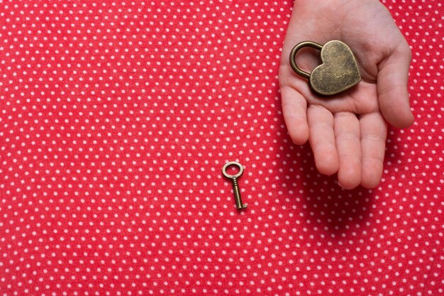 Mano sujetando una cerradura y llave en forma de corazón sobre fondo rojo.