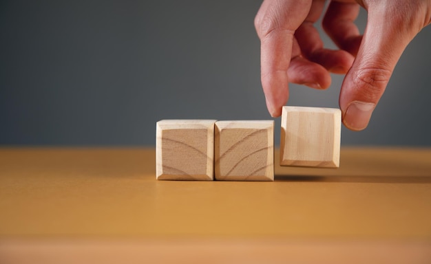 Mano sujetando cubos de bloque de madera en blanco sobre fondo de mesa, concepto de negocio