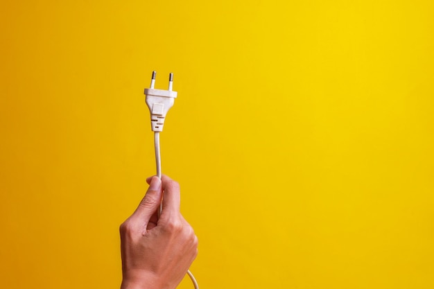 Foto mano sujetando el enchufe eléctrico blanco aislado sobre fondo amarillo con espacio de copia ahorre energía y ea