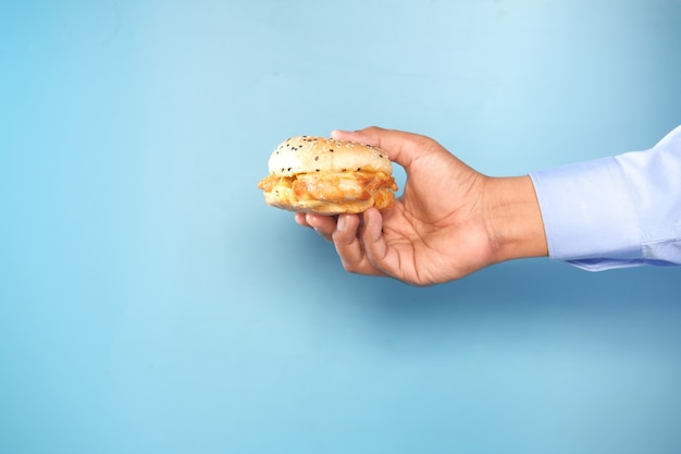 Foto mano sujetando la hamburguesa de ternera contra backgrund azul con espacio de copia