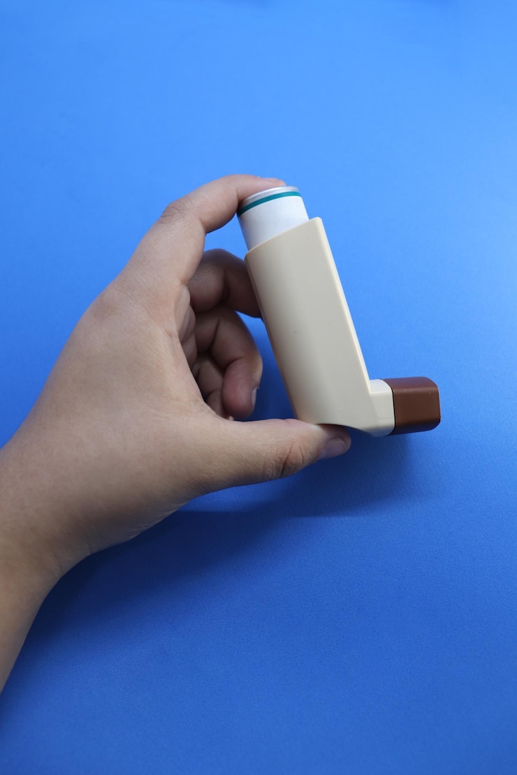 Foto mano sujetando el inhalador sobre fondo azul.