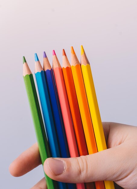 Mano sujetando lápices de colores colocados sobre un fondo blanco
