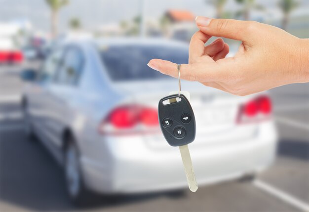 Mano sujetando una llave de coche con coche metálico en el fondo