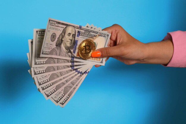 Mano sujetando moneda dólar y bitcoin sobre fondo azul.