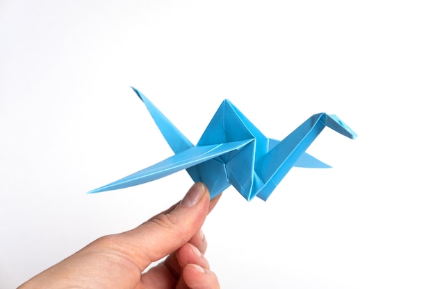 Mano sujetando pájaro azul de papel aislado sobre fondo blanco Grúa de papel como símbolo de paz Origami de papel Manualidades de papel con niños