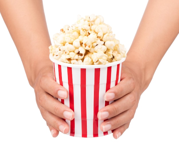 Mano sujetando palomitas de maíz en balde rayado aislado sobre fondo blanco.