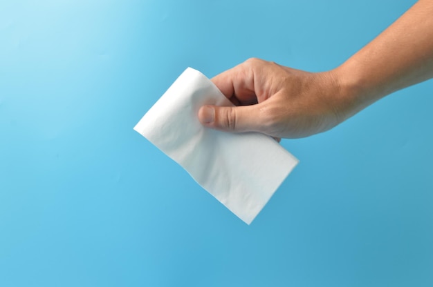 Mano sujetando un pañuelo de papel blanco aislado en un fondo azul Concepto de salud y seguridad higiénica
