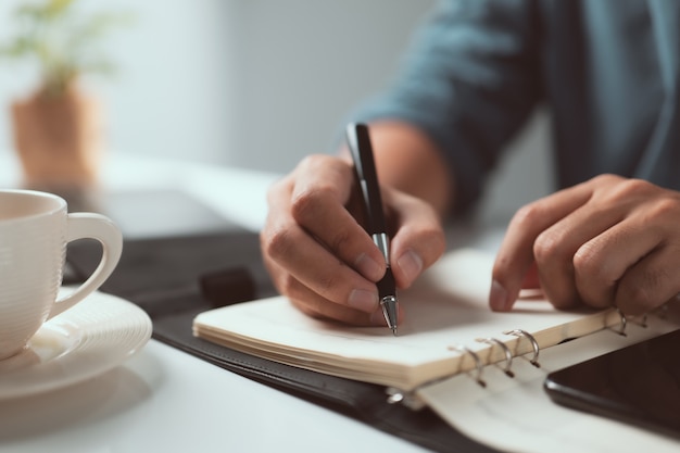 Mano sujetando la pluma y escribiendo una nota sobre la mesa Lista de verificación Aviso Recuerde el concepto de planificación