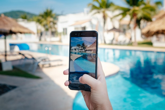 Mano sujetando el teléfono en el fondo de la piscina en la cámara de fotos del hotel en la pantalla cerrar la mano sujetar el teléfono inteligente tomar una foto de las vacaciones de verano