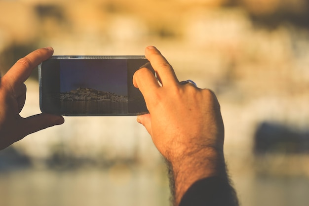 Mano sujetando el teléfono móvil tomando fotografías del casco antiguo de Ibiza