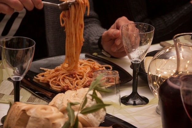 Mano sujetando el tenedor y entregando un bocado de espagueti a ragu en una mesa durante un almuerzo