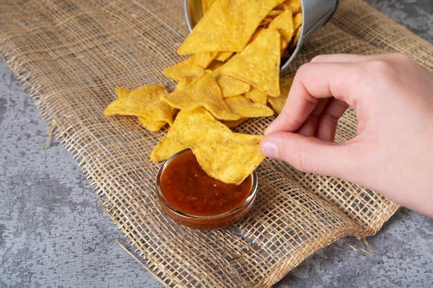 La mano sumerge los chips de maíz nacho en la salsa picante de tomate Bocadillo mexicano