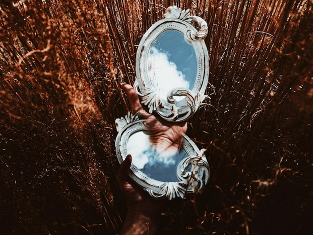 Mano surrealista sosteniendo un espejo con el reflejo de las nubes