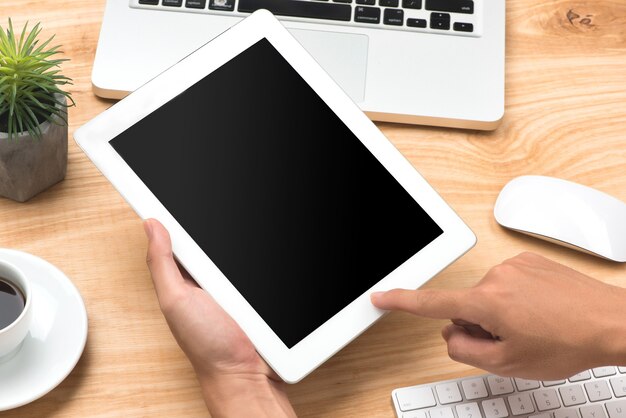 Mano con tableta digital con pantalla en blanco en la mesa de trabajo de escritorio