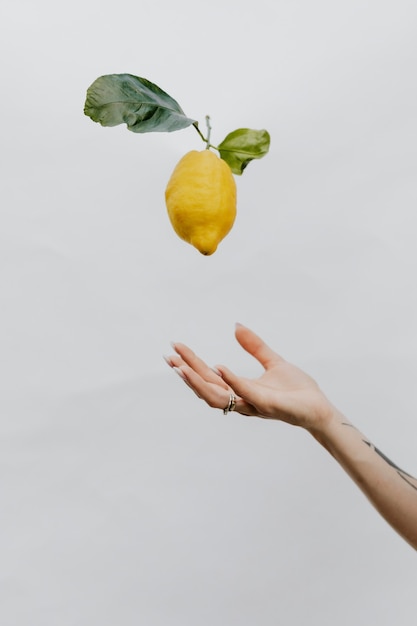 Mano tatuada arrojando un limón en un cielo gris