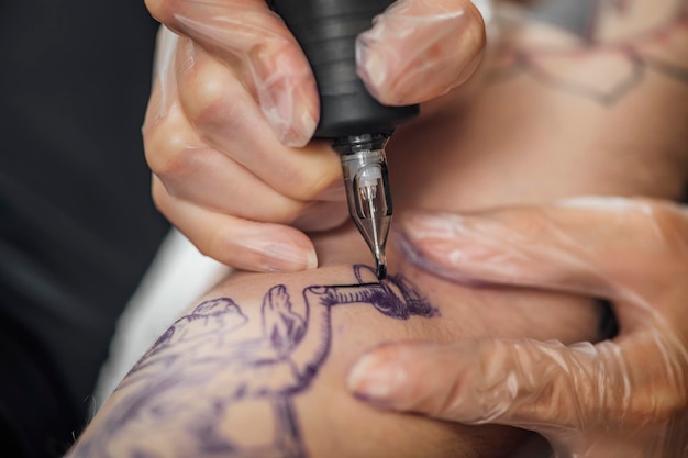 Mano de Tatuador en Guantes de Goma Dibujar un Tatuaje con Pistola Eléctrica de Tatuaje Primer Plano