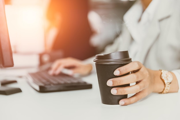 Mano en la taza de café en el escritorio de la oficina gente de negocios bebiendo café de una taza de papel para un buen concepto de trabajo