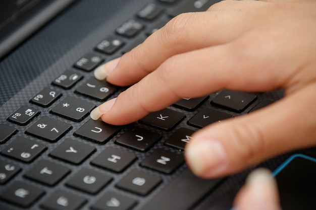 Mano en el teclado negro de una computadora escribiendo texto