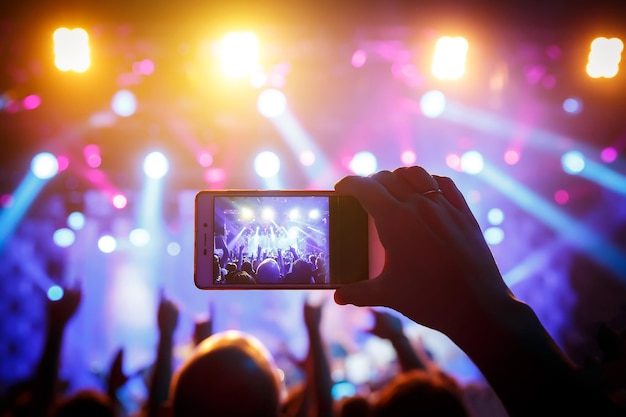 Mano con un teléfono inteligente graba un festival de música en vivo y toma una foto del escenario del concierto