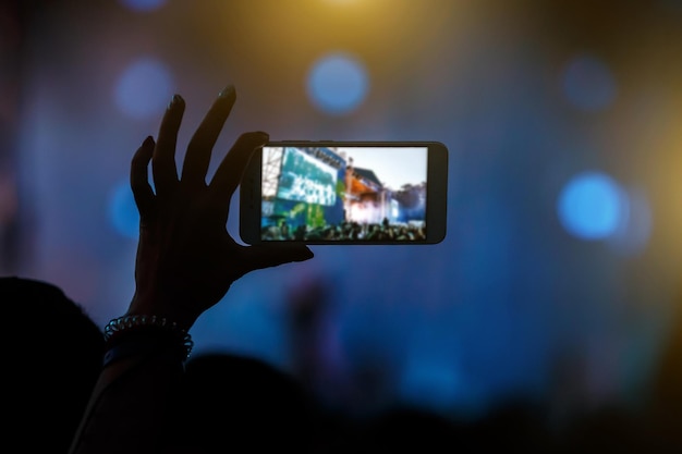 Foto mano con un teléfono inteligente graba un festival de música en vivo y toma una foto del escenario del concierto