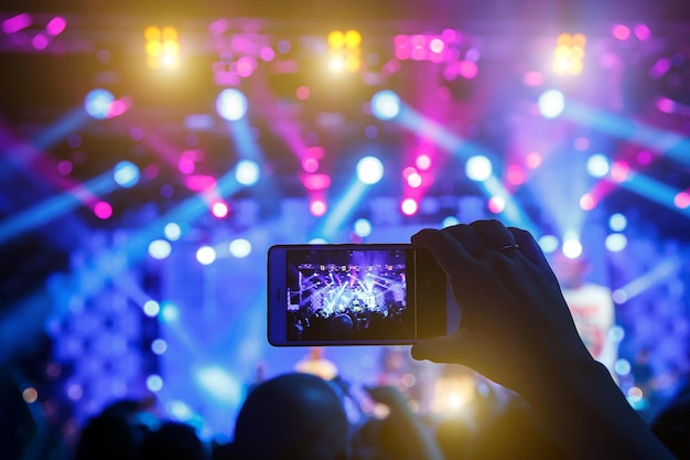 Mano con un teléfono inteligente graba un festival de música en vivo y toma una foto del escenario del concierto