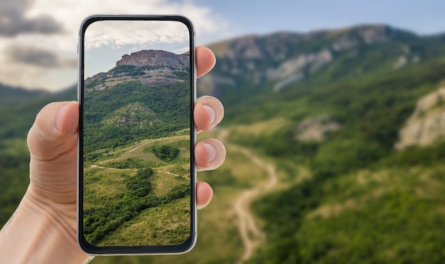 Una mano con un teléfono inteligente móvil y tomando una fotografía de paisaje.