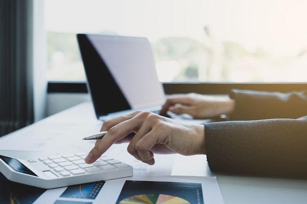 La mano del tenedor de libros de las empresarias utiliza la calculadora y la computadora portátil en el escritorio blanco en la oficina de trabajo.