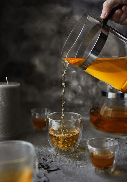 Una mano con una tetera vierte té hirviendo en una taza durante el desayuno. Copa con vapor