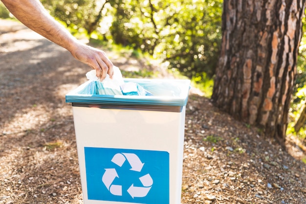 Foto mano tirando basura en el cubo de basura en el bosque