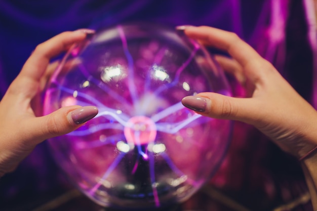 Foto mano tocando una bola de plasma con suaves llamas azul magenta.