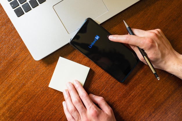 Mano tocando un teléfono inteligente con la aplicación Linkedin en un escritorio