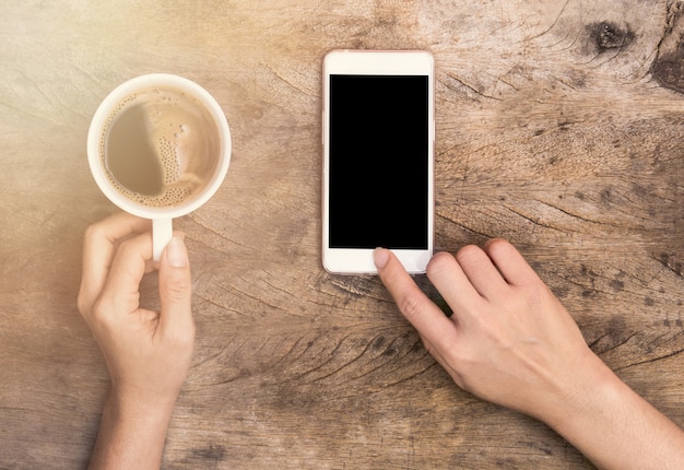 Mano tocando el teléfono inteligente y sosteniendo la taza de café