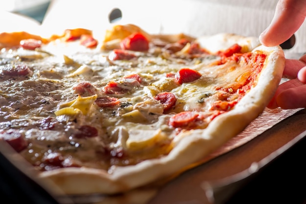 La mano toma una rebanada de pizza fresca y saca queso derretido de la caja.