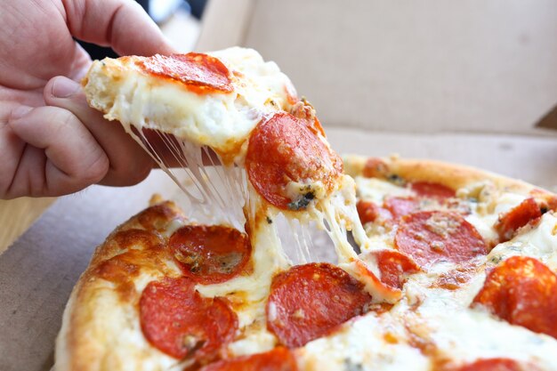 La mano toma una rebanada de pizza de queso caliente de la caja.