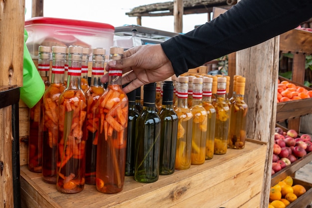 Mano tomando una botella de alcohol con infusión de frutas en un mercado