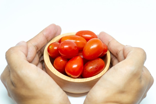 Mano con tomate en cuenco de madera.