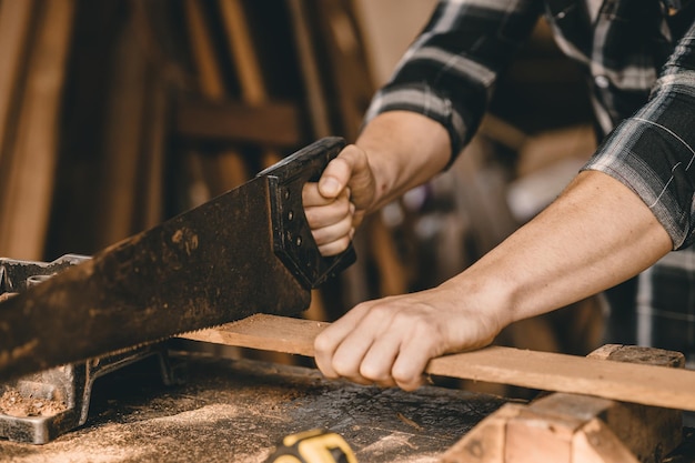 Mano de trabajador constructor masculino de primer plano con sierra para madera para aserrar madera en el taller de muebles.