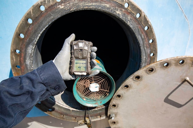 Mano del trabajador que sostiene la inspección del detector de gas prueba de gas de seguridad en el tanque de acero inoxidable de la boca de inspección delantera para trabajar dentro del confinamiento