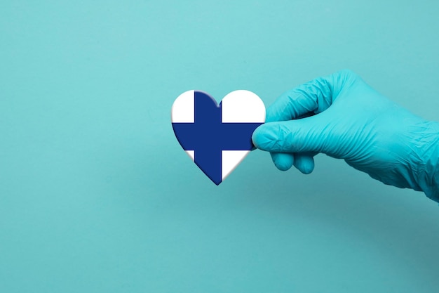 Mano de trabajadores médicos con guante quirúrgico con corazón de bandera de finlandia