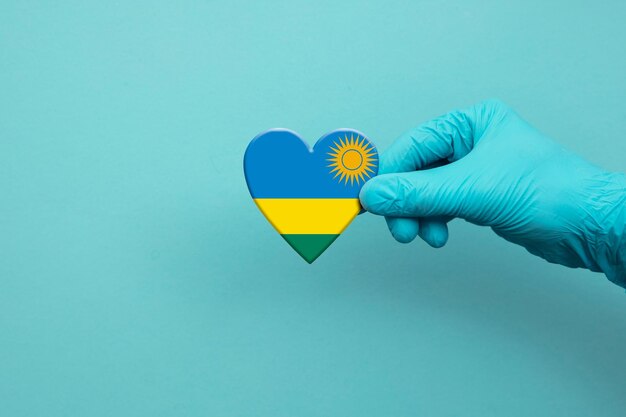 Mano de trabajadores médicos con guante quirúrgico con corazón de bandera de ruanda