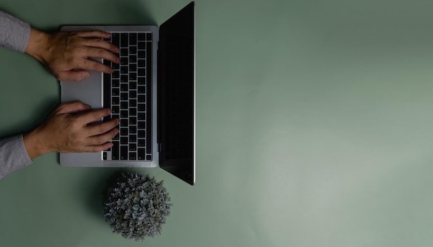 Mano usando computadora portátil y flor sobre fondo verde Vista superior copia espacio en blanco