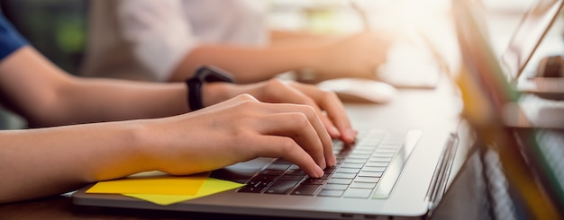 Mano usando la computadora portátil con el teclado de prensa en la oficina. proporción del banner para anuncios.