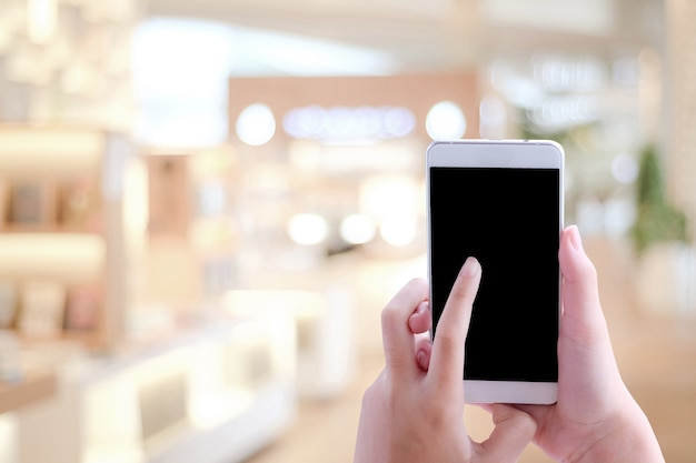 Mano usando teléfono inteligente sobre la tienda de desenfoque con fondo de luz bokeh