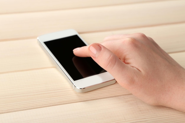 Mano usando un teléfono móvil inteligente en el fondo de la mesa de madera