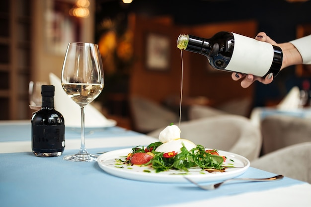 Mano vertiendo aceite de oliva en ensalada de burrata italiana