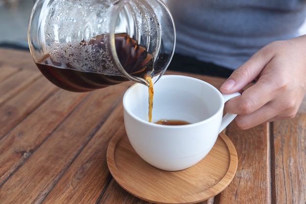 Mano vertiendo café por goteo en una taza blanca sobre la mesa de madera vintage