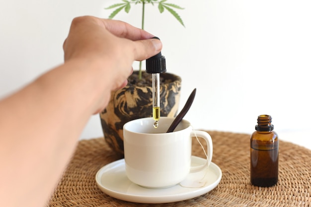 Mano vertiendo gotas de aceite de cáñamo en infusión de desayuno