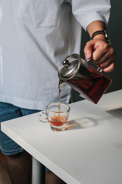La mano vertiendo el té en la taza sobre la mesa