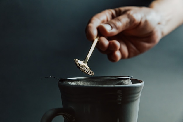 Una mano vieja preparando un té sobre un fondo oscuro y tonos oscuros